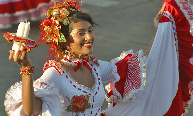 Traditional Colombian dancer in red and white dress holding candles during the Barranquilla Carnival