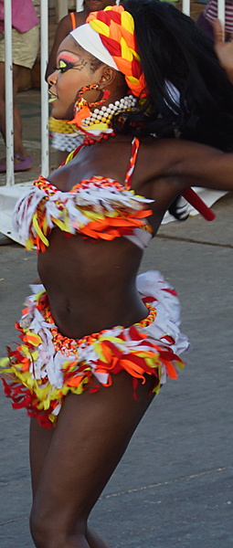 Afro-Caribbean Carnival Dancer in Motion Energetic Afro-Caribbean woman dancing in a vibrant red, yellow, and white feathered costume with colorful makeup and braided headwrap during the Barranquilla Carnival parade