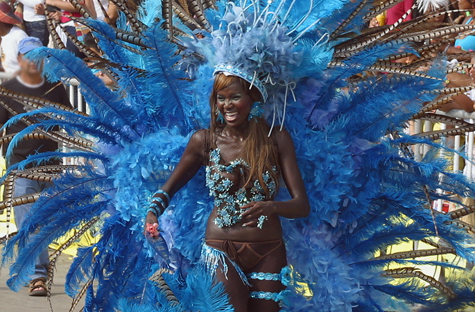Joyful Barranquilla Carnival dancer in an elaborate blue feathered costume and headdress, smiling during the parade