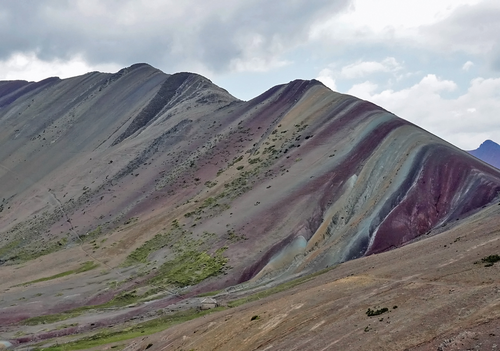 Sloped Andean ridge in Peru painted with wide, multicolored stripes of maroon, teal, and sandy yellow caused by natural mineral deposits