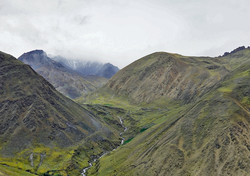 Cordillera Vilcabamba Peru Narrow glacial valley flanked by steep, grass-covered slopes and distant jagged peaks of the Vilcabamba range