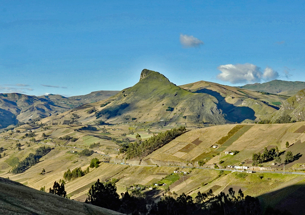 Andes Highlands of Cotopaxi A striking green peak towers above a mosaic of cultivated plots in the highlands of Cotopaxi Province, with winding roads and distant ridgelines under a bright sky