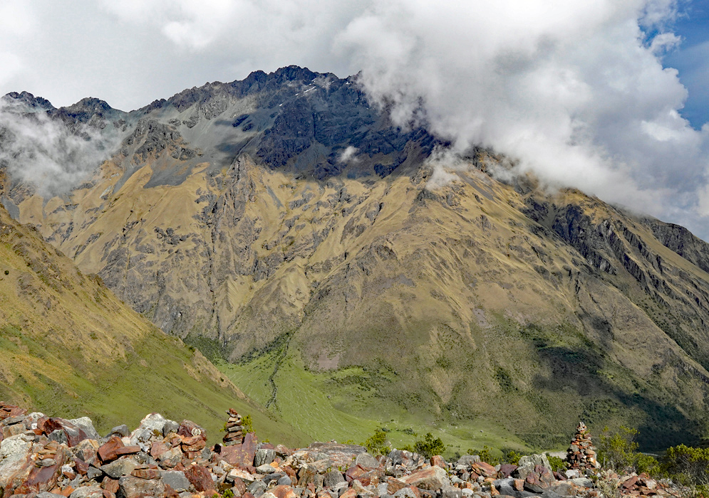 Andes Mountains Humantay Golden-brown mountains of the Andes rising steeply under a cloudy sky with cairns made of reddish stones in the foreground near Humantay