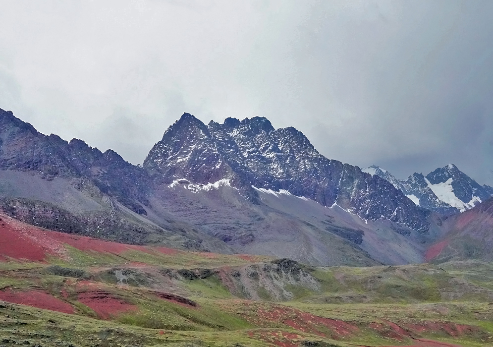 Snow-capped peaks of the Ausangate Massif tower over a vibrant alpine valley of red and green in the high Andes of Peru