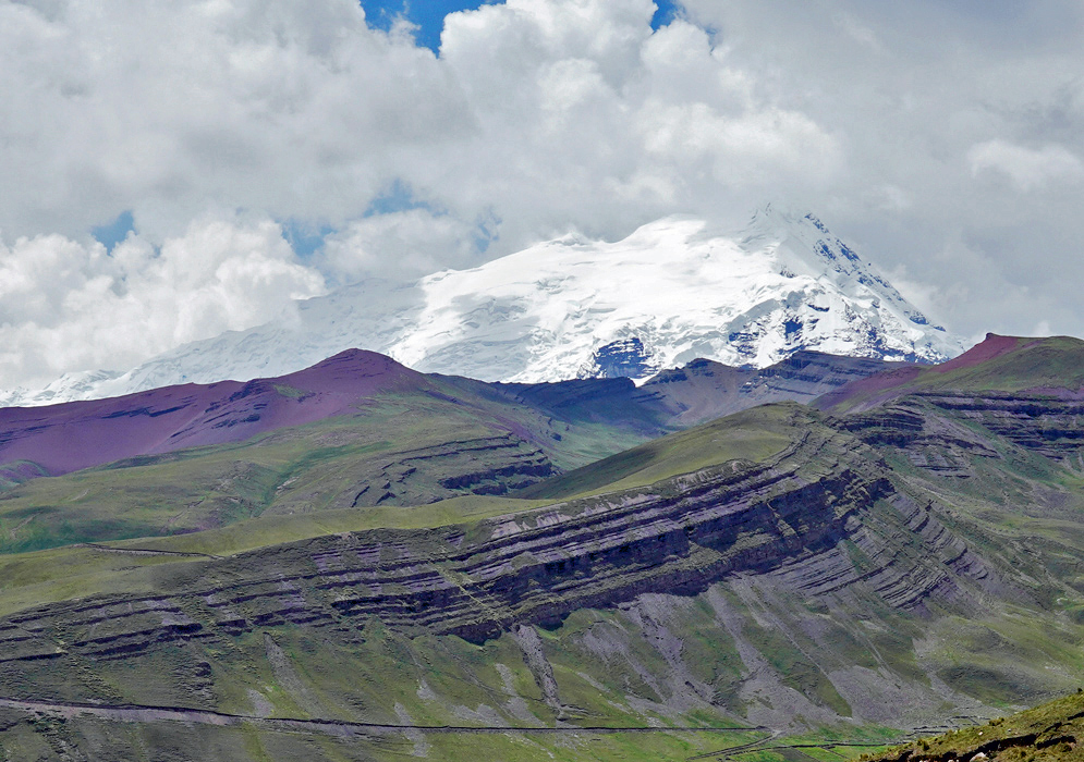 Ausangate Mountain Cordillera Vilcanota Snow-capped Ausangate Mountain towers above steep purple and green striped ridges in the Cordillera Vilcanota, partially framed by dramatic clouds
