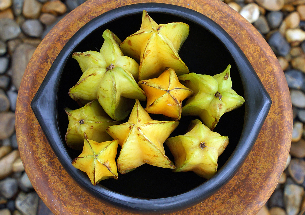 Eight yellow, green and orange star-shape Averrhoa carambola fruits in a black bowl