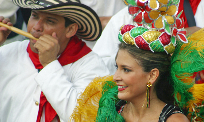 Colombian man playing a traditional flute next to a smiling carnival woman in colorful headpiece and costume during Barranquilla Carnival