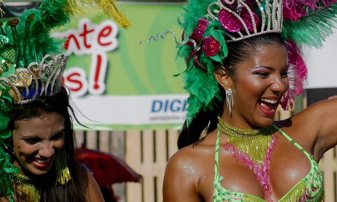 Two joyful carnival dancers in vibrant green costumes and feathered crowns smiling and celebrating during the Barranquilla Carnival