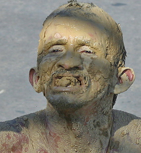 Carnival performer completely covered in drying mud with eyes closed and an expressive smile