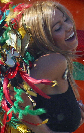 Joyful Carnival Dancer with Feathered Wings Blonde woman laughing and dancing in a black costume adorned with colorful feathers and metallic decorations during the Barranquilla Carnival celebration
