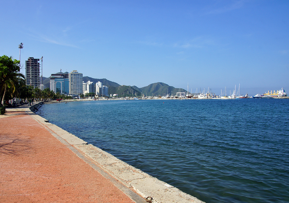 Beach walkway leading to the boat harbor with green mountains in the background and blue skies