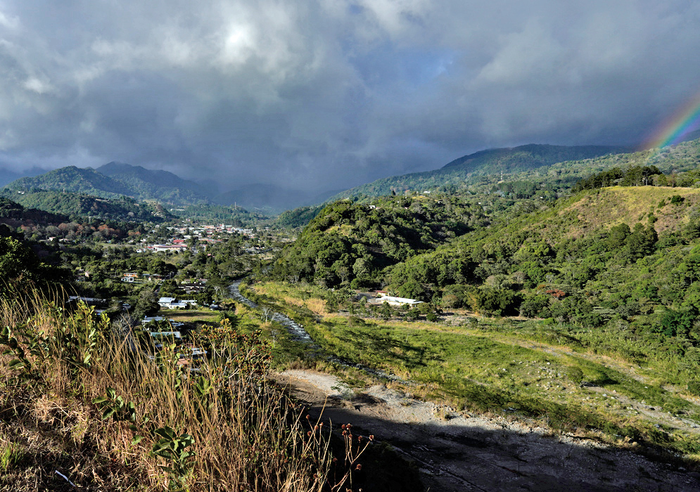Boquete Panama Scenic Valley A panoramic view of Boquete, Panama, showing a lush green valley with scattered homes and buildings under a stormy sky and a faint rainbow on the horizon