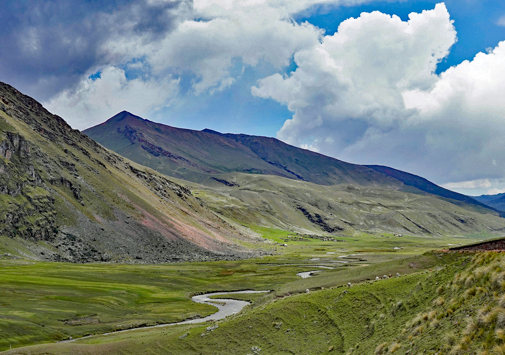 A serpentine mountain stream cuts through the remote highlands of Canchis Province, with sharp ridges and dramatic clouds rising above the peaceful valley