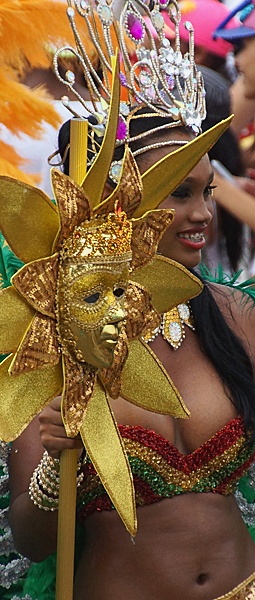 Carnival Beauty Holding Golden Sun Mask Smiling woman in a glittering red and green costume with a jeweled crown, holding a decorative golden sun-shaped mask during the Barranquilla Carnival parade