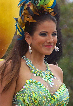 Barranquilla Carnival Performer in Green Costume Elegant woman wearing a bright green and turquoise costume with reflective embellishments and a feathered headdress, smiling proudly during the Barranquilla Carnival parade