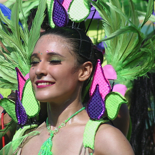Smiling Barranquilla Carnival dancer with green face paint and elaborate headpiece decorated with neon feathers and sequins