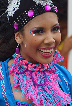 Smiling Carnival Performer in Blue Vibrant Barranquilla Carnival dancer with bright pink and blue face gems, a woven multicolor necklace, and a jeweled headdress, smiling joyfully in a glittering blue costume