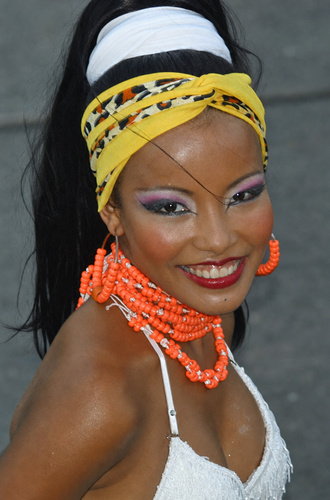 Smiling Colombian carnival dancer with vibrant makeup, orange beads, and a yellow headband at the Barranquilla Carnival