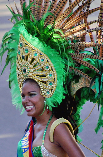 Smiling Barranquilla Carnival performer wearing an elaborate green and gold feathered headdress and sash during the parade