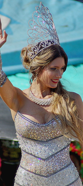 Smiling carnival queen in a silver sequin dress and ornate crystal crown waving during the Barranquilla Carnival parade