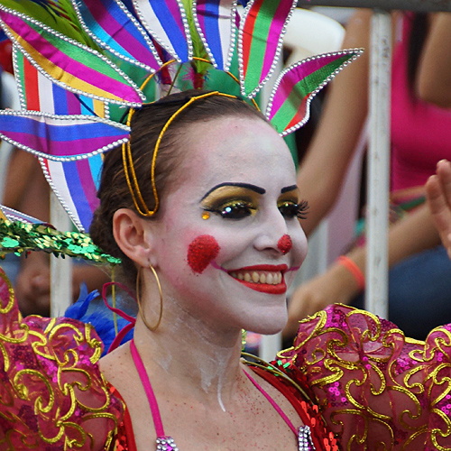 Smiling Colombian woman in colorful clown makeup and vibrant costume performing during Barranquilla Carnival parade