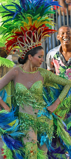 Elegant woman in a shimmering green costume with rainbow feathered wings and crown performing during the Barranquilla Carnival parade
