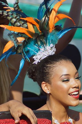 Radiant young woman at Barranquilla Carnival wearing a jeweled crown with orange and blue feathers, smiling in the parade
