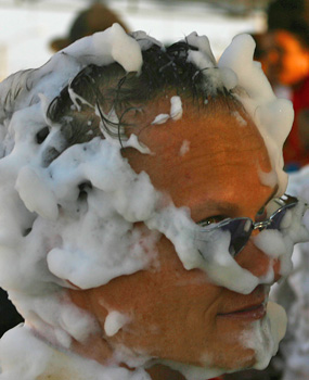 Smiling Colombian woman with foam on her face during Barranquilla Carnival, wearing a pink top and festive earrings