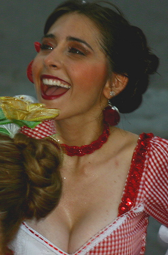 Laughing Colombian woman in red checkered traditional dress with sequins, wearing bold makeup and floral earrings during carnival celebration
