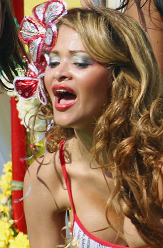 Smiling Colombian carnival woman with long wavy hair, wearing a festive outfit and sparkling red and silver floral headpiece, mid-celebration
