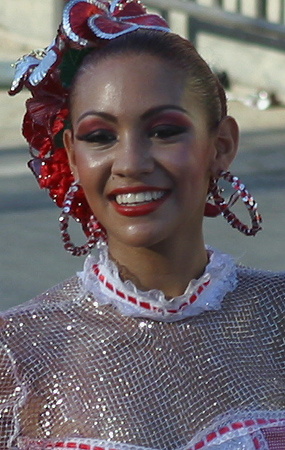 Barranquilla Carnival Dancer in Red and White Smiling young woman wearing a red and white costume with sequin mesh fabric, hoop earrings, and floral hair accessories during the Barranquilla Carnival parade