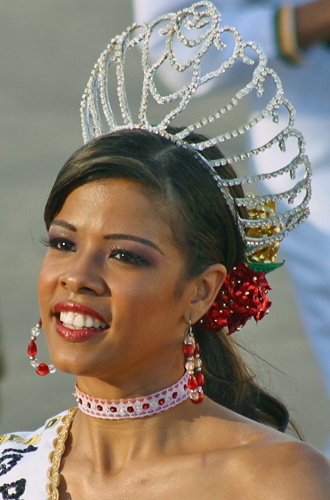 Elegant young woman at Barranquilla Carnival wearing a silver rhinestone crown and red floral accessories, smiling proudly during the parade