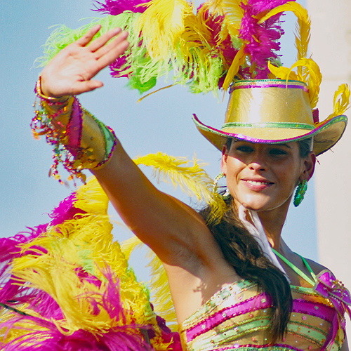 Smiling Colombian woman in a yellow hat and colorful feathered costume waving during the Barranquilla Carnival parade