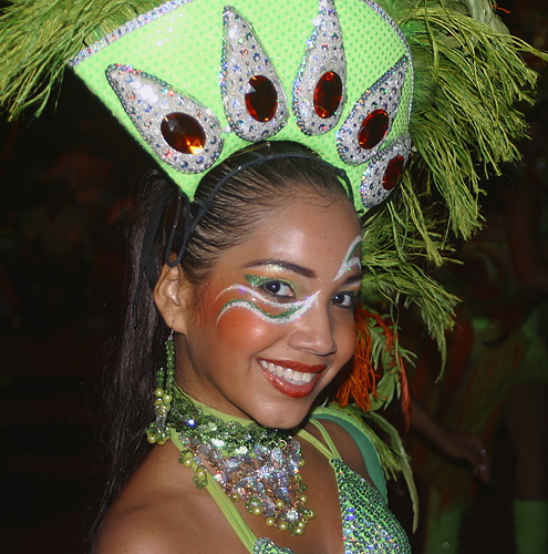 Smiling Barranquilla carnival dancer in a sparkling green costume and elaborate gem-studded headdress during a night parade