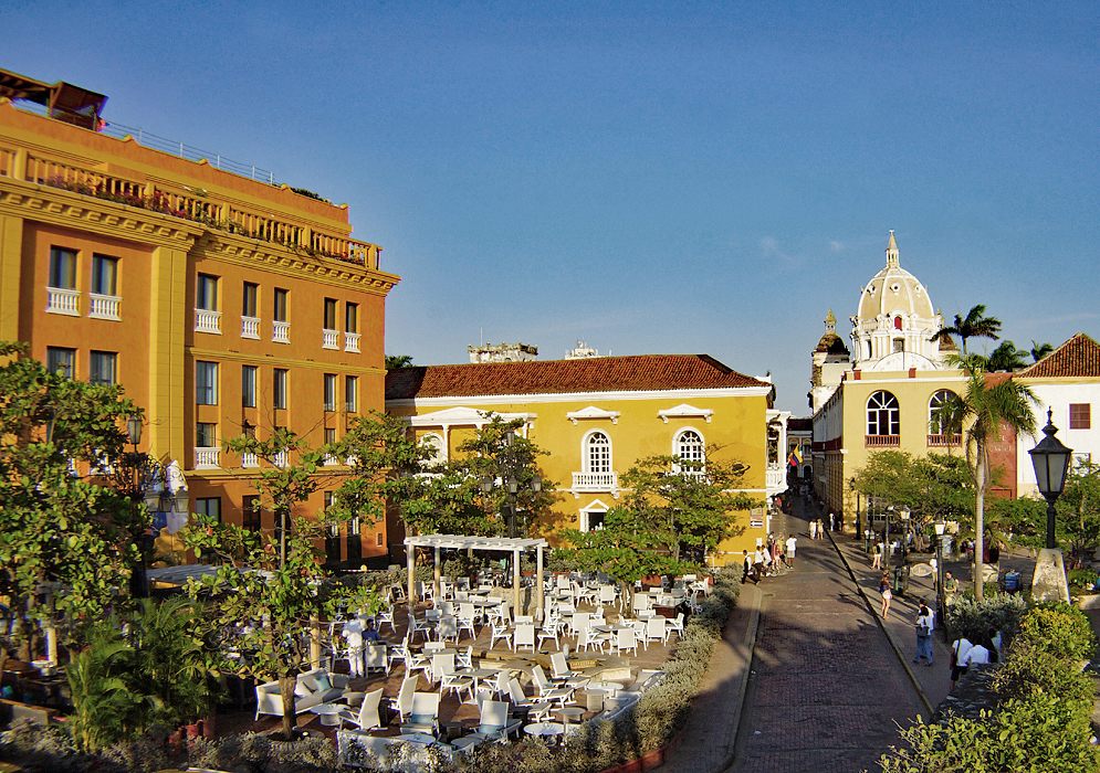 A large dining plaza surrounded by orange and yellow buildings during the late afternon