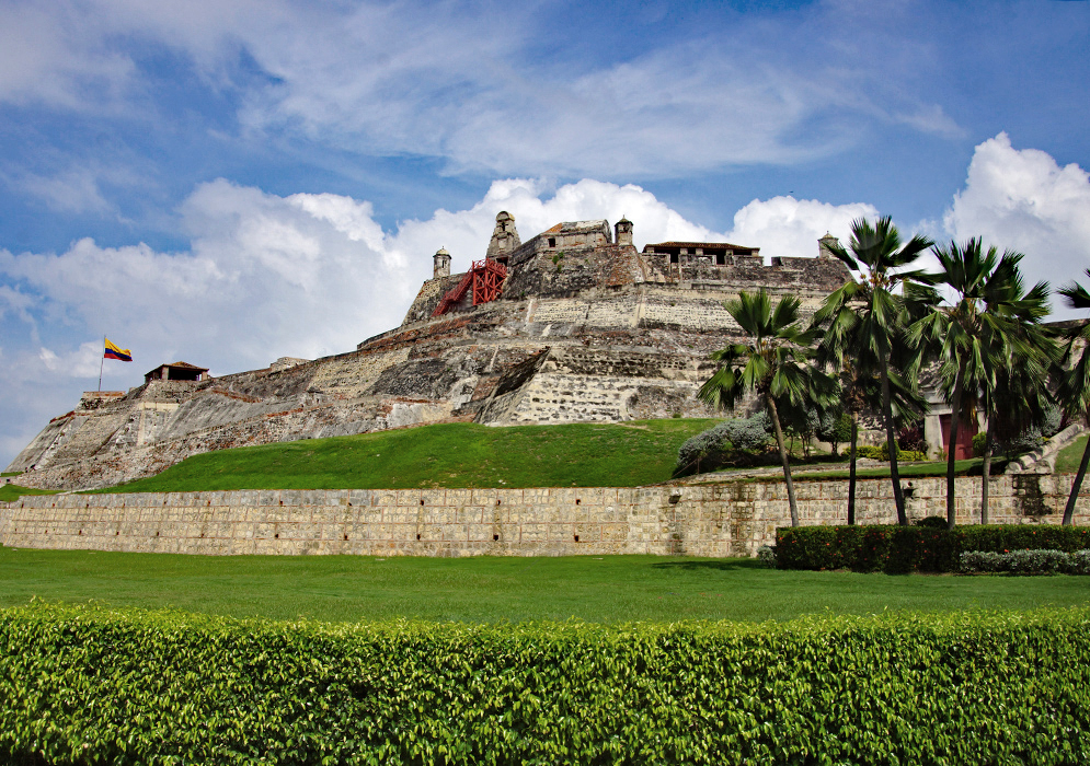 A large old fort surrounded by grass under blue sky and white clouds