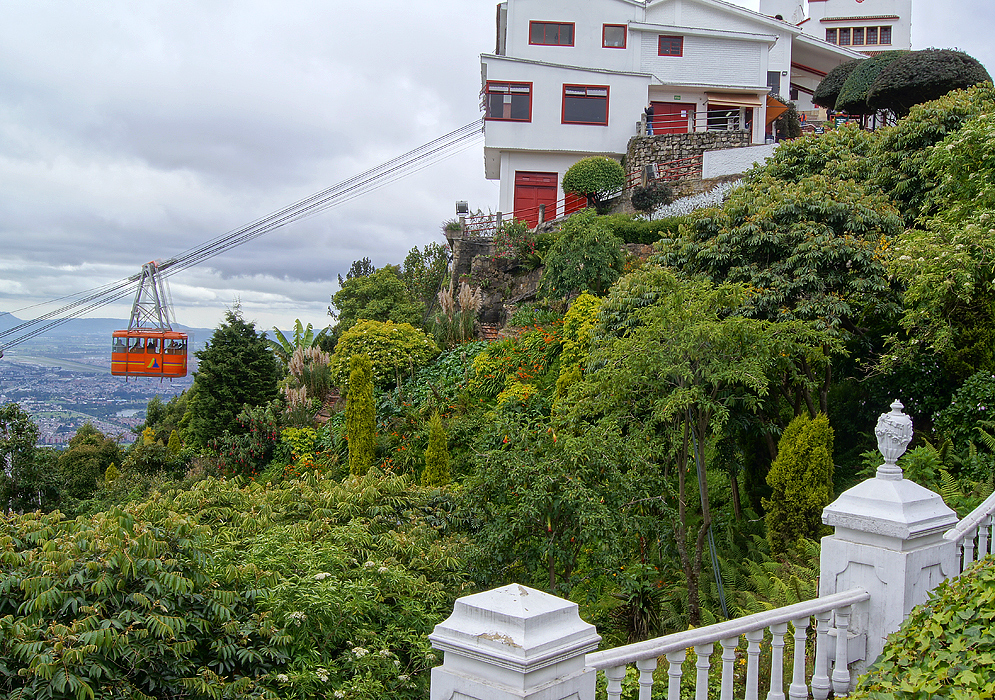 An orange cable car close to the white cable station with a flowering garden in the foreground