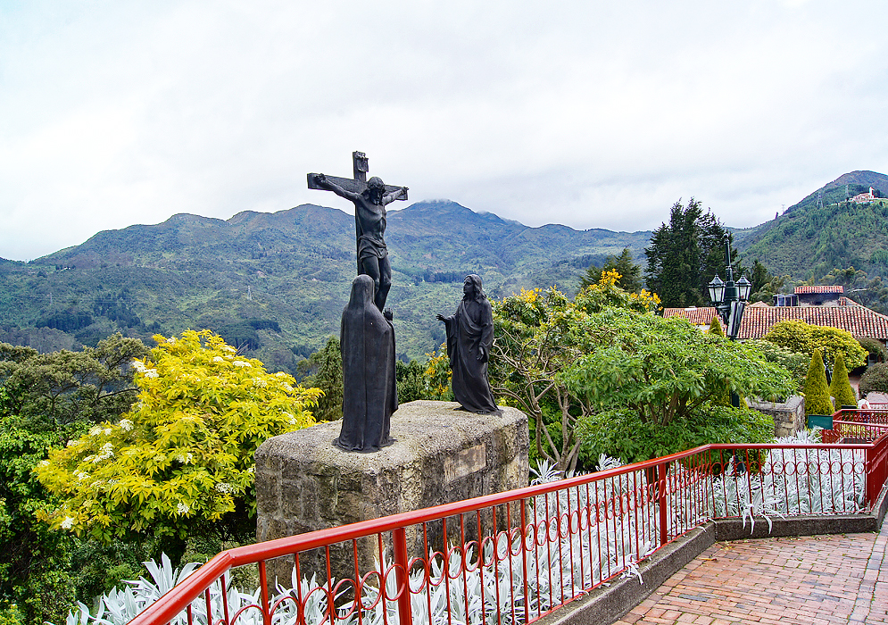 A statue of Jesus Christ on a stone block with the Andes mountains in the background under cloudy skies