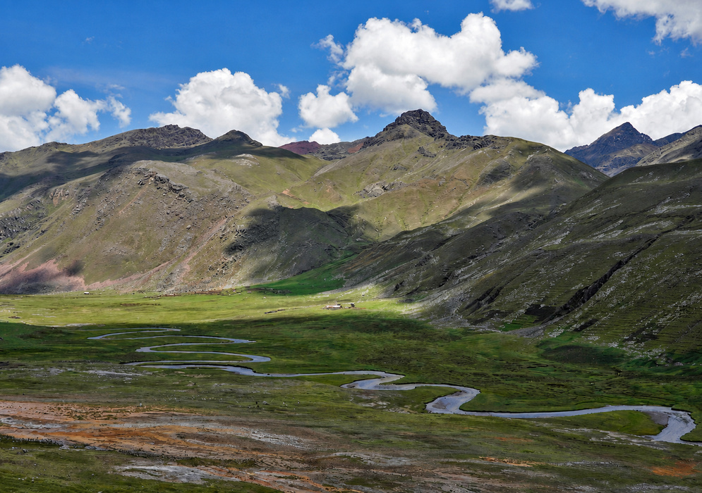 A winding river flows through the lush green Chilca Valley, surrounded by rugged Andean peaks and scattered sheep grazing on the slopes