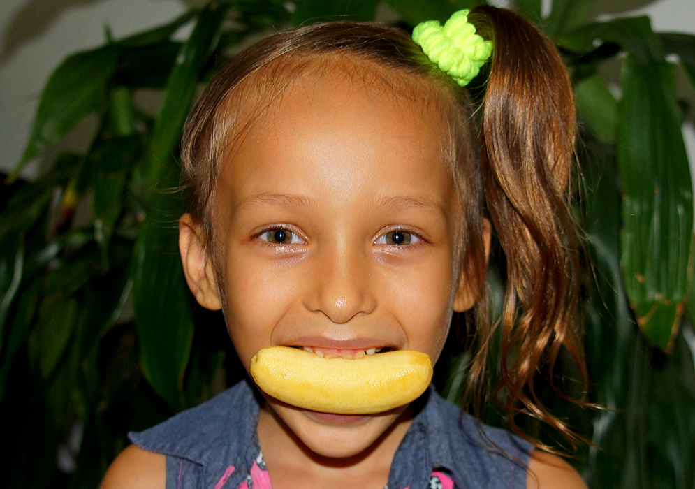 A five-year old girl with a horizontal small banana in her mouth