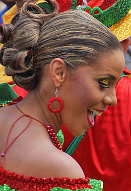 Dancing Barranquilla Beauty Side view of an elegant Colombian woman with golden-highlighted hair in an updo, wearing festive makeup and red hoop earrings, joyfully dancing in a vibrant red and green costume during the Barranquilla Carnival