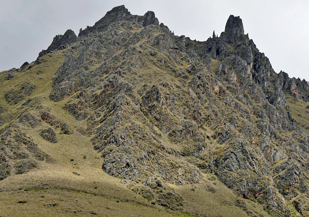 Cordillera Vilcabamba Ridge Jagged volcanic ridge of the Cordillera Vilcabamba with dry grass slopes and exposed dark rock formations rising into a cloudy sky