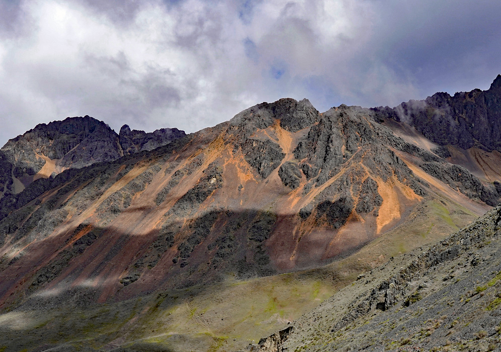 Cordillera Vilcanota Mountain Range Rugged peaks of the Cordillera Vilcanota with streaks of orange mineral deposits contrasting against a deep blue sky and scattered clouds