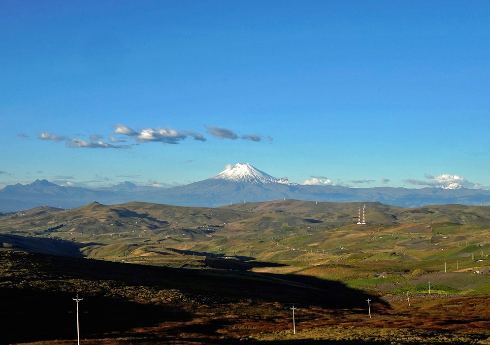Cotopaxi Volcano Across the Andean Páramo A broad open landscape of the Andean páramo stretches toward the base of Cotopaxi Volcano, which is partially covered in snow under a deep blue sky
