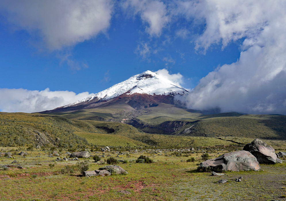 Cotopaxi Volcano In Ecuador Cotopaxi Volcano stands tall with its glacier-covered peak contrasting against the green valley and large boulders in the foreground
