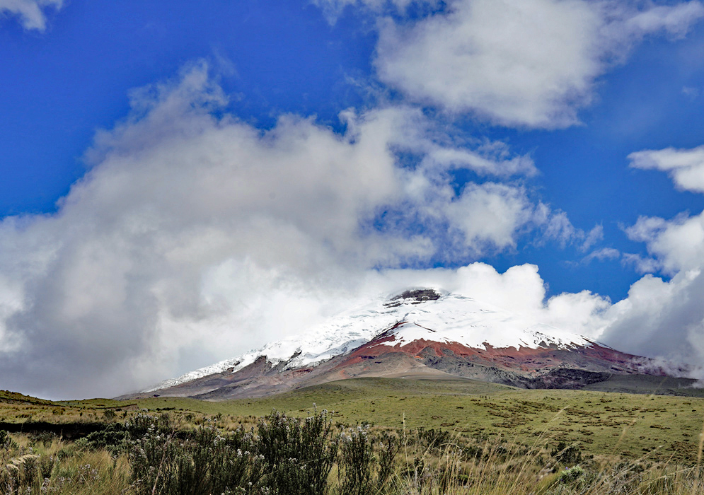 Rocky Terrain Beneath Cotopaxi Large volcanic boulders and red soil dot the vibrant green terrain below Cotopaxi’s towering white peak