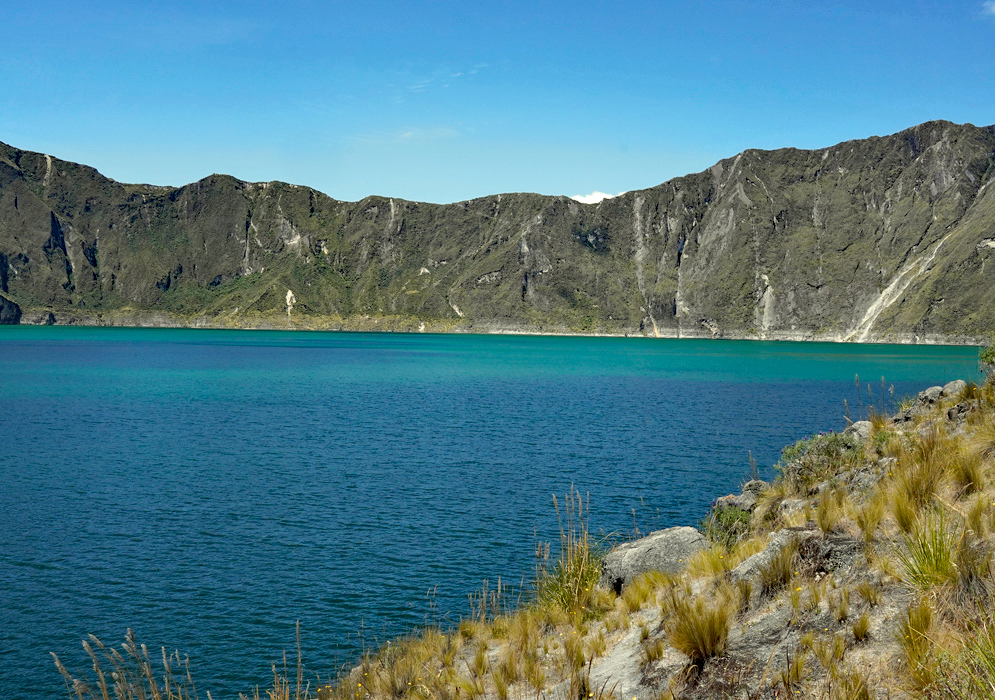 Quilotoa Lake Emerald View Emerald tones of Quilotoa Lake seen from a rocky slope, with cliffs rising in the background under a blue sky