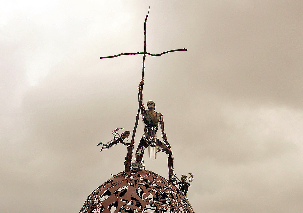 A man made of metal holding a cross