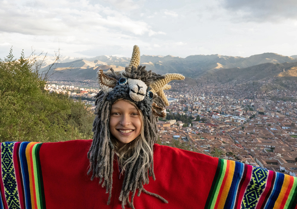 Overlooking Cusco in Traditional Dress Young girl in traditional Peruvian costume with colorful woven poncho posing with a panoramic view of Cusco city behind her
