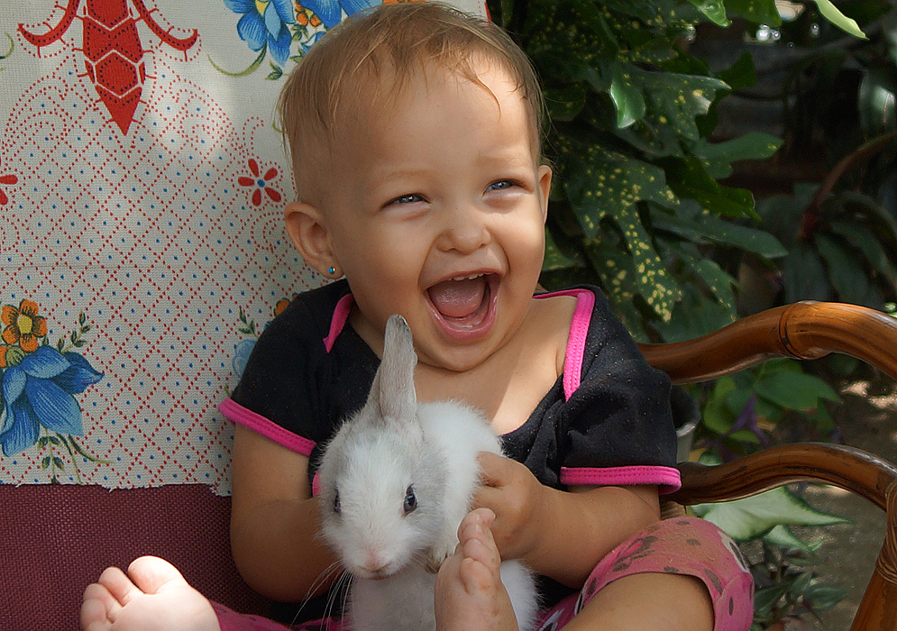 Joyful baby girl hold a white baby rabbit